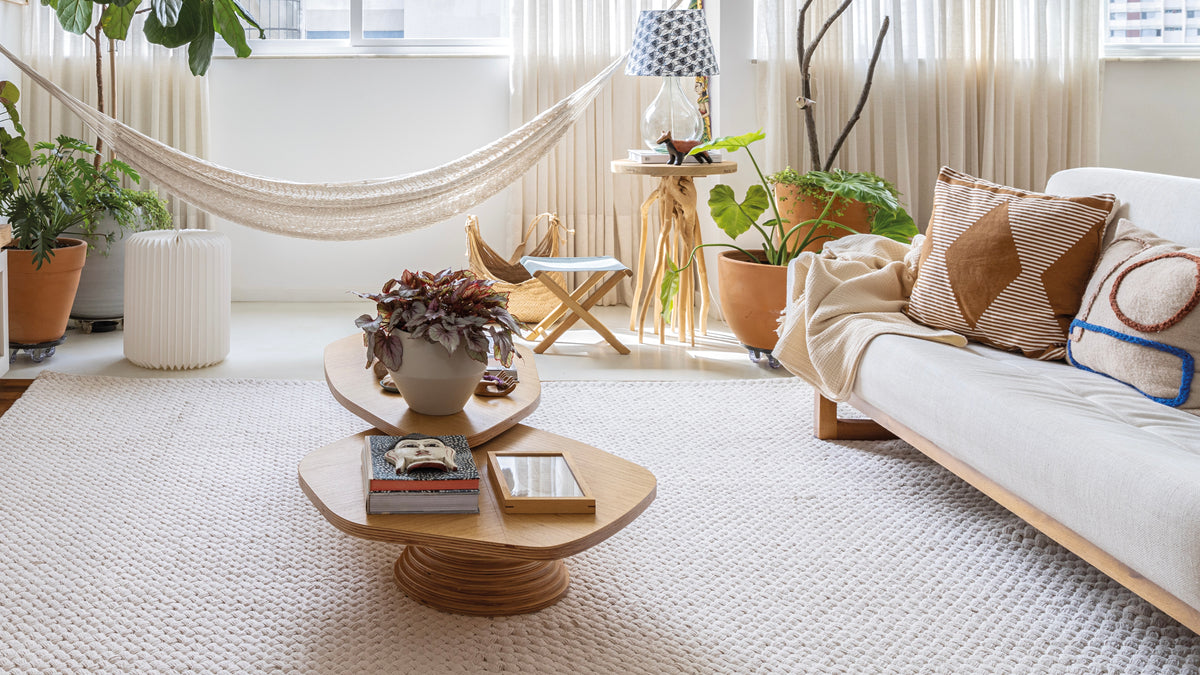 Como deixar o ambiente aconchegante com tapete claro texturizado, sofá neutro, madeira, plantas e luz natural na sala.