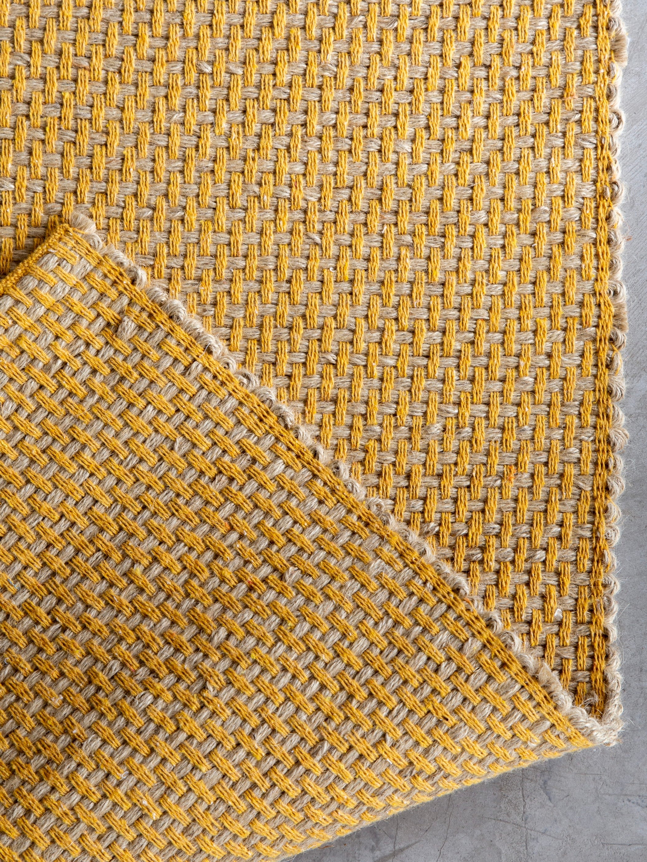 Detalhe da borda do Tapete Milah amarelo em juta natural e algodão colorido.