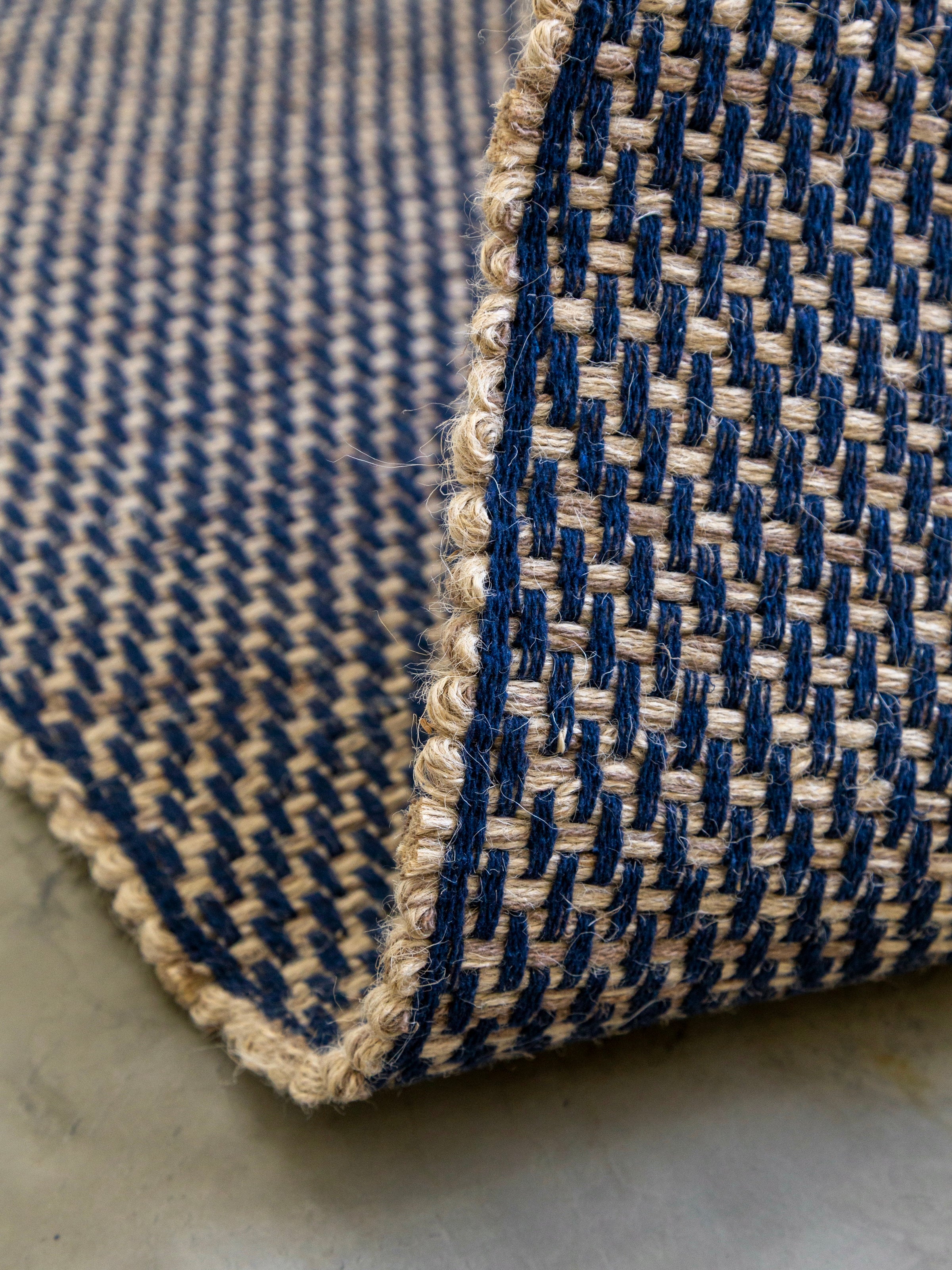 Detalhe da borda do Tapete Milah azul-marinho com trama artesanal contrastante.