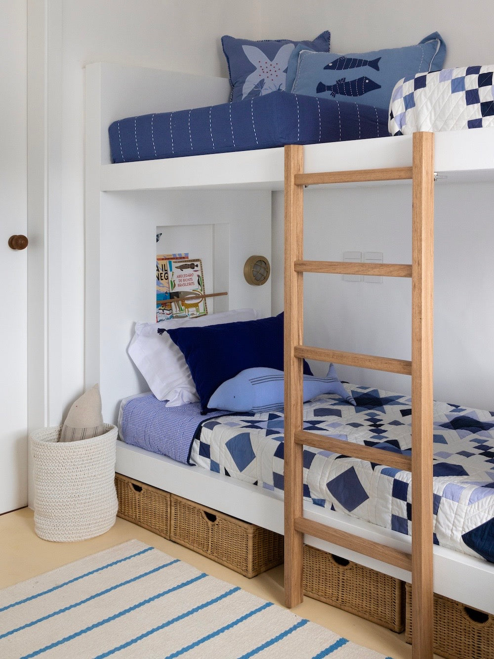 Tapete Pontal de fundo cru com listras azuis ao pé de beliche com roupa de cama azul e branca.