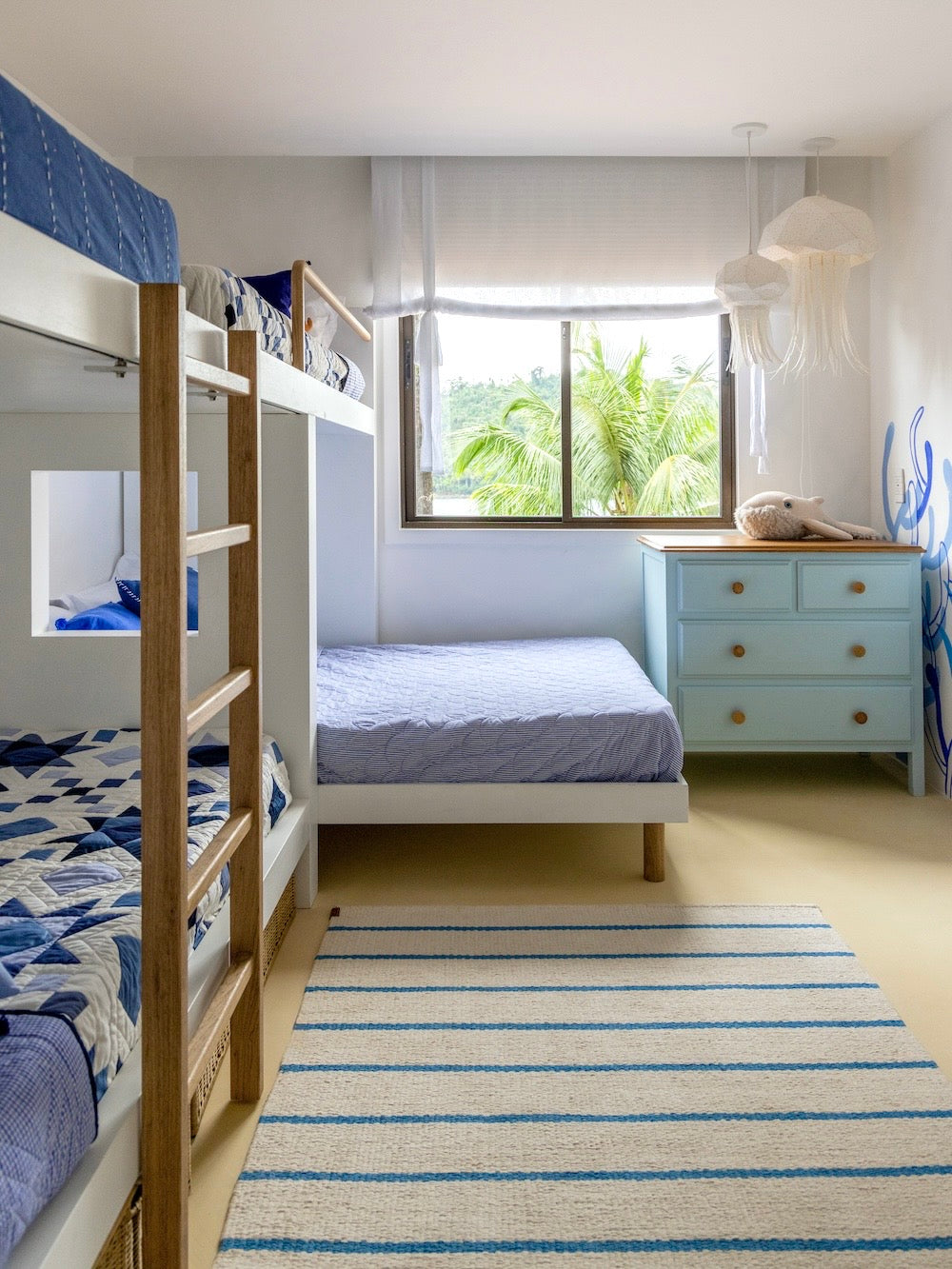 Tapete Pontal com listras azuis em quarto com beliche, janela e cômoda azul-clara.