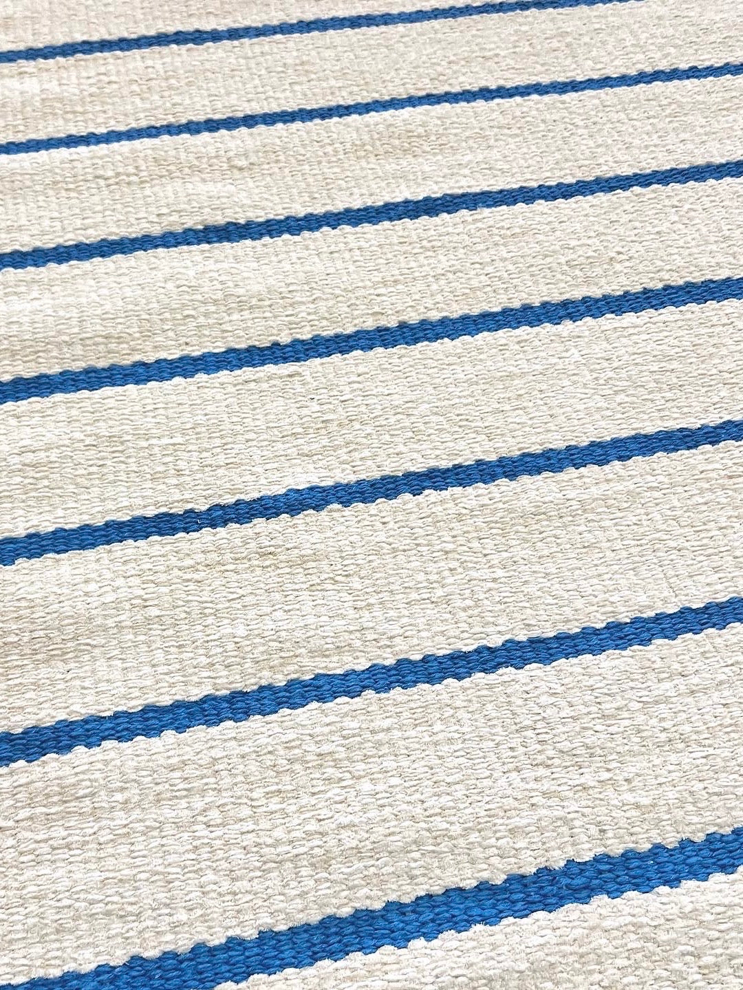 Detalhe da trama do Tapete Pontal de fundo cru com listras azuis.