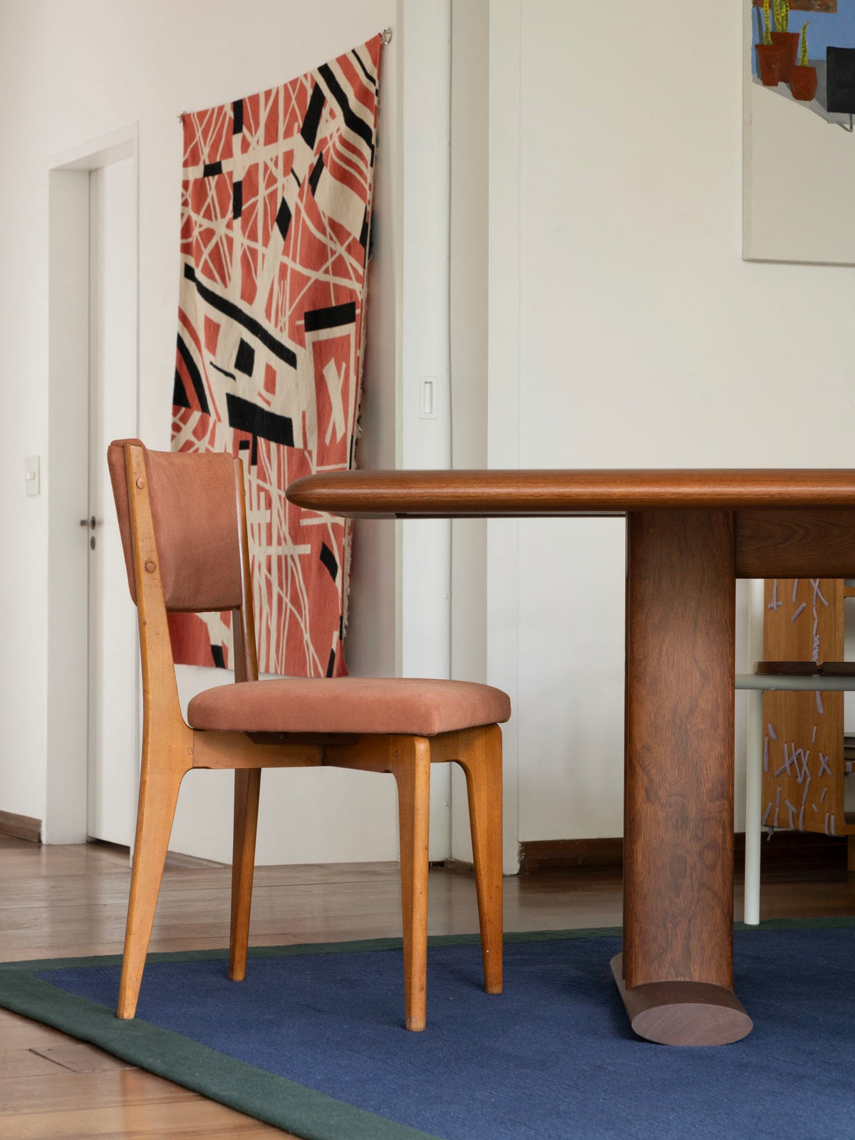 Detalhe do Tapete Duo azul com borda verde da Leva Oficina, sob mesa de madeira e cadeira vintage estofada em rosa, em sala de jantar contemporânea.