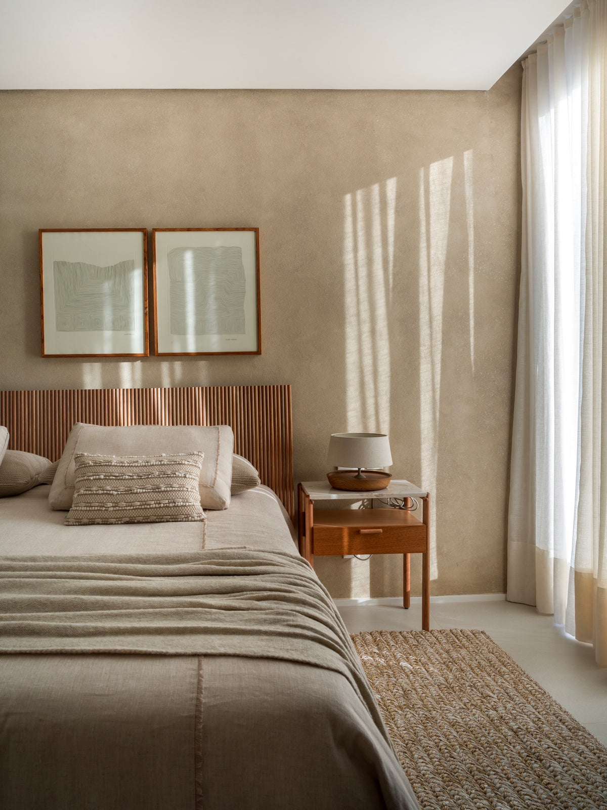 Tapete Alva Mix Camelo ao lado da cama em quarto com cabeceira de madeira e cortinas claras.