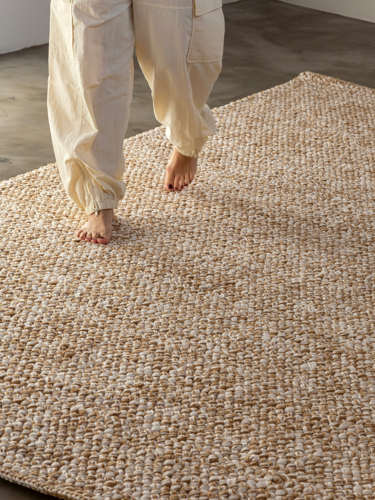 Pessoa caminhando descalça sobre o Tapete Alva Soft, com trama em tons de bege e branco.