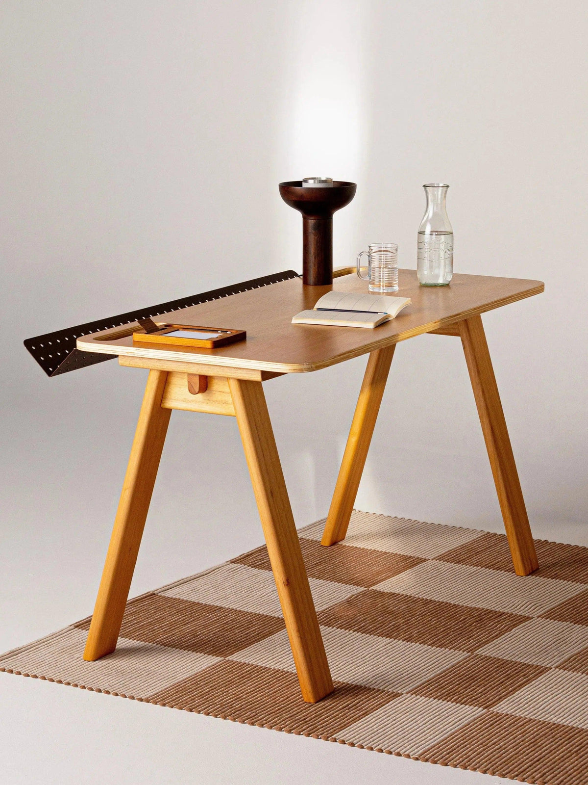 Tapete Chroma quadriculado cru e camelo sob mesa de madeira com livros e objetos decorativos.