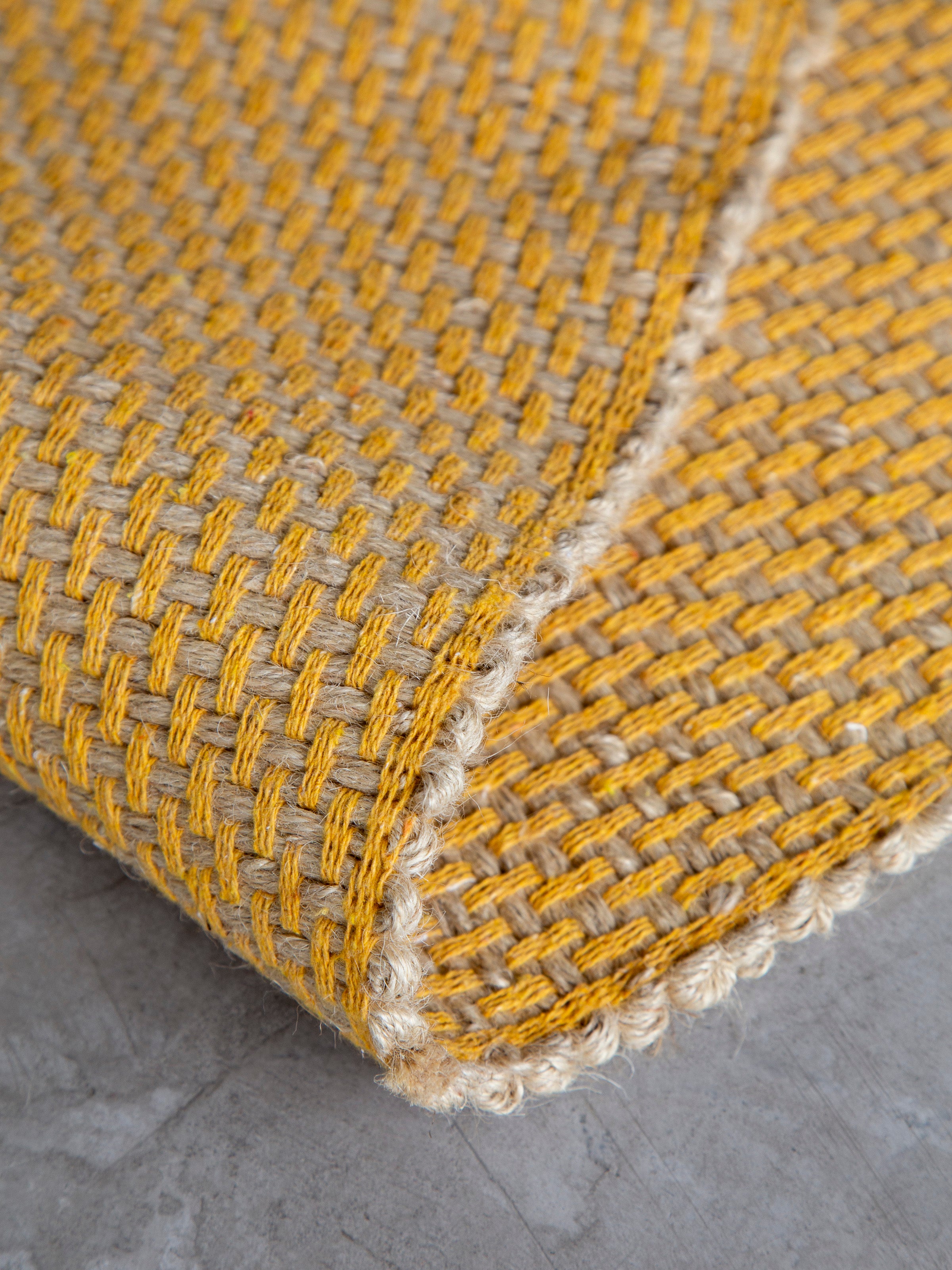 Detalhe do canto do Tapete Milah amarelo com trama artesanal.