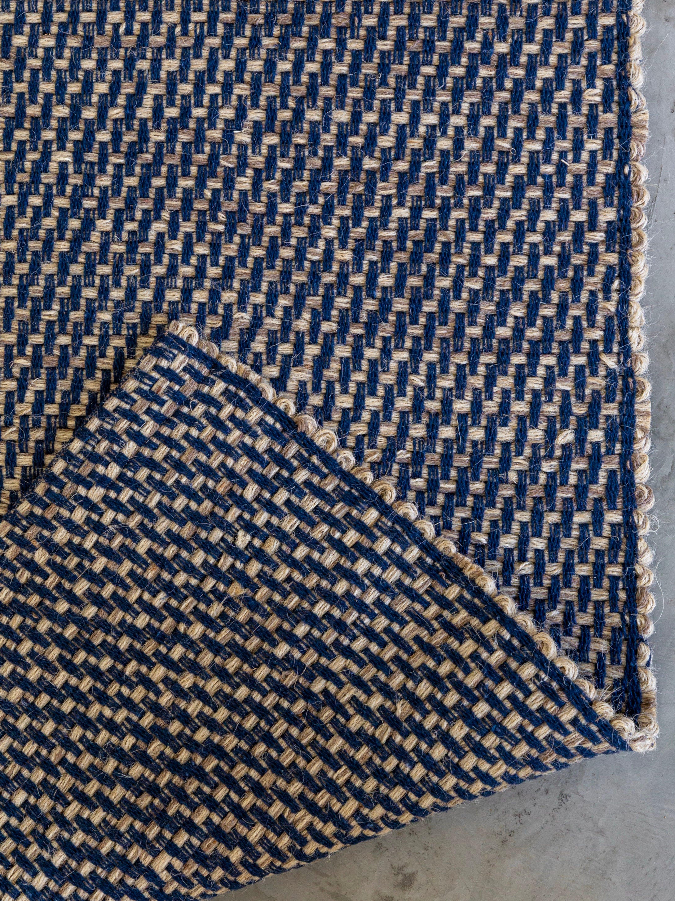 Detalhe do canto do Tapete Milah azul-marinho em juta e algodão.