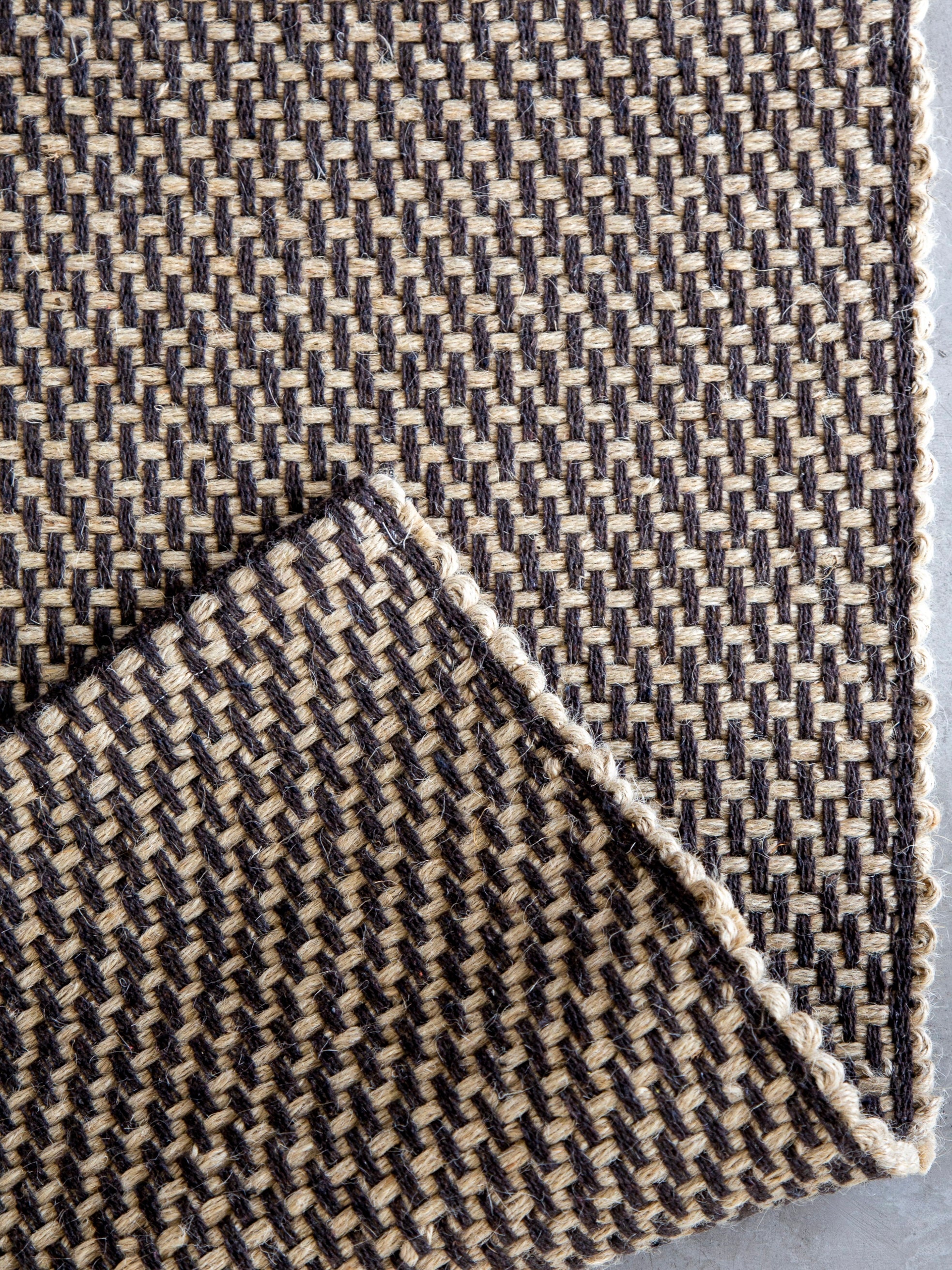 Detalhe do canto do Tapete Milah café em juta natural e algodão.