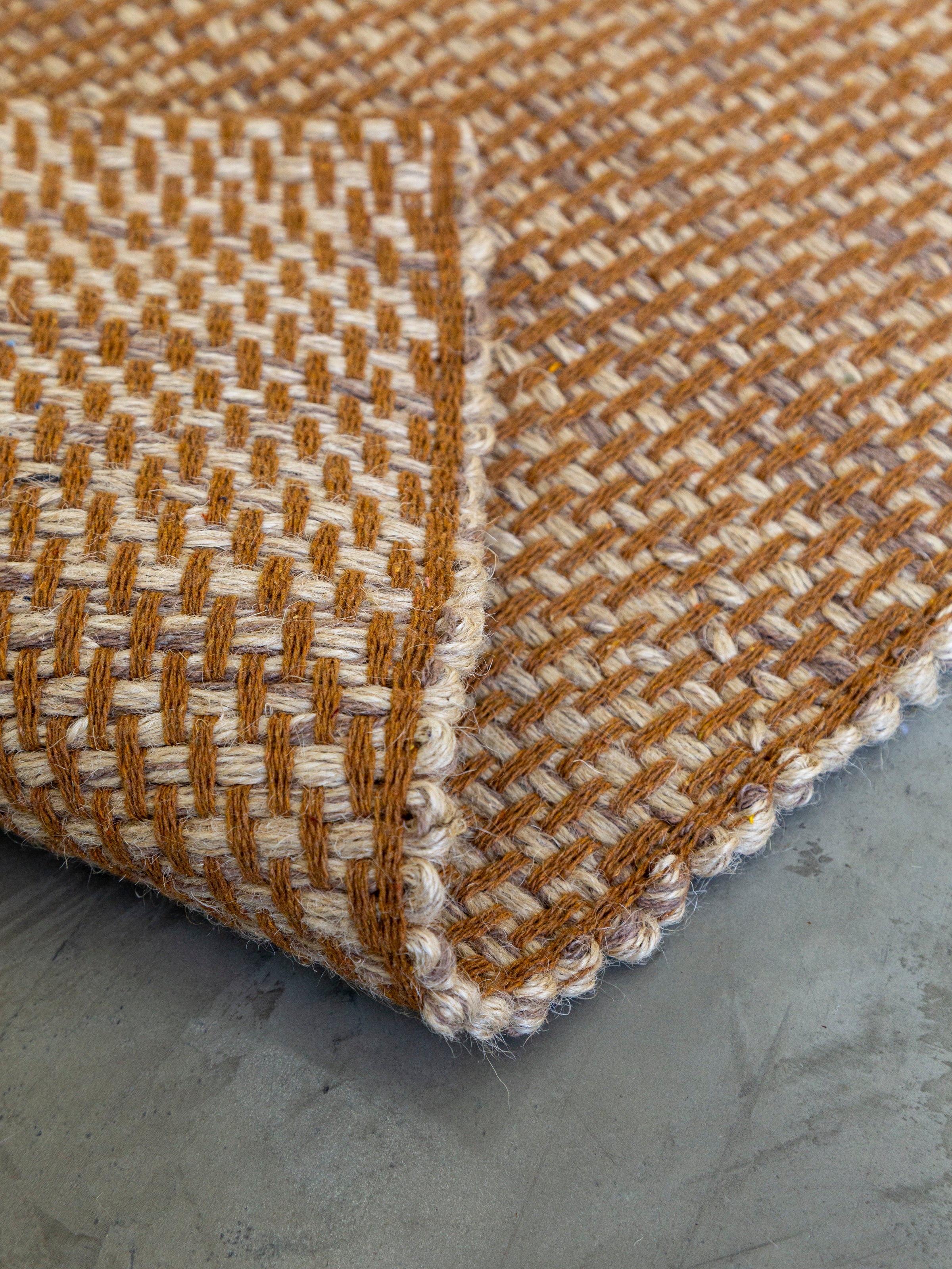 Detalhe da borda do Tapete Milah camelo com trama artesanal contrastante.