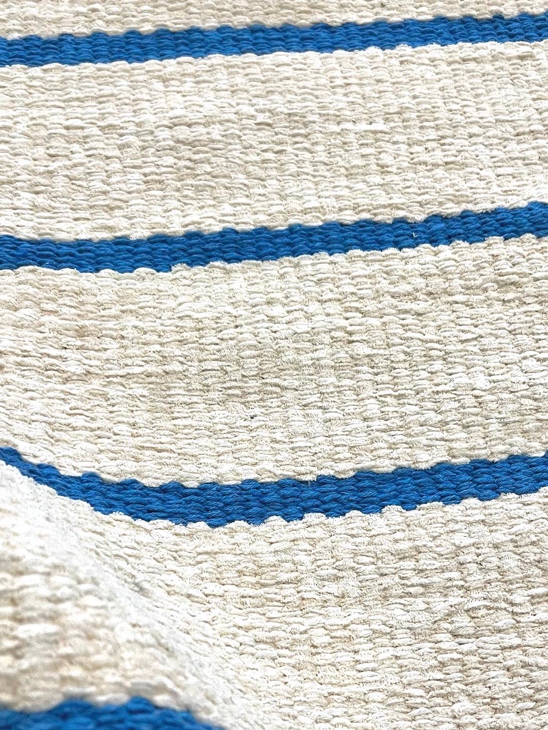 Aproximação da textura do Tapete Pontal de fundo cru com listras azuis e uma dobra no tecido.